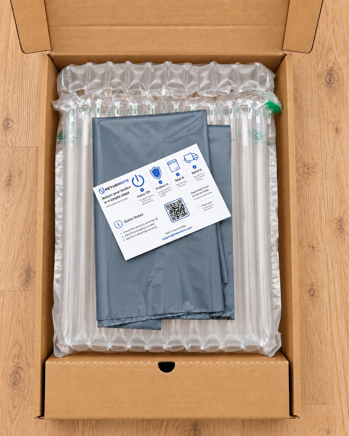 Laptop Return Kit: open cardboard box lined with inflatable air-column padding, with a grey mailing bag and a ReturnKits instruction card inside