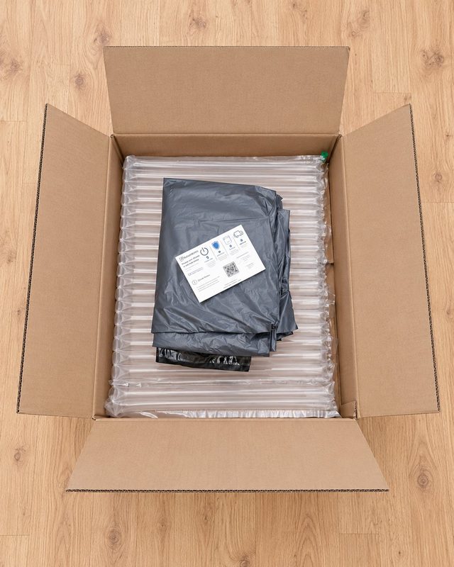 Monitor Return Kit: large open cardboard box lined with inflatable air-column padding, with grey mailing bags and a ReturnKits instruction card inside